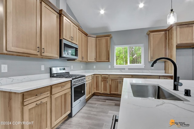 kitchen with light stone countertops, appliances with stainless steel finishes, light hardwood / wood-style floors, sink, and hanging light fixtures