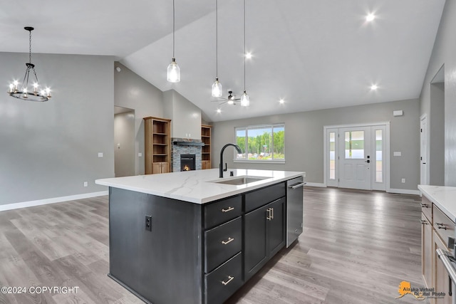 kitchen featuring a stone fireplace, an island with sink, dishwasher, hanging light fixtures, and sink