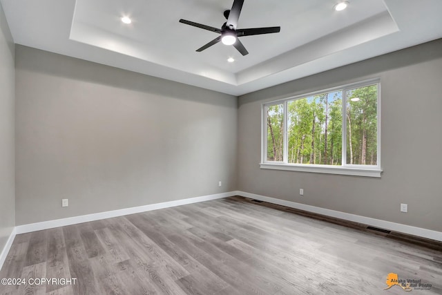 spare room featuring ceiling fan, a tray ceiling, and light hardwood / wood-style flooring