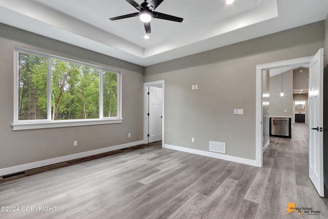 unfurnished room with ceiling fan, light hardwood / wood-style flooring, and a raised ceiling