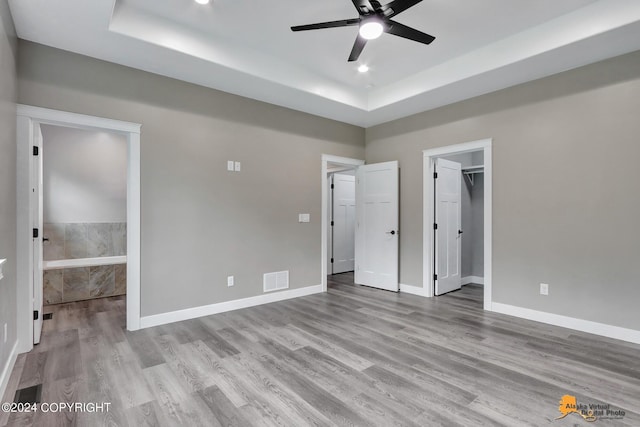 unfurnished bedroom featuring a spacious closet, ensuite bathroom, ceiling fan, a raised ceiling, and a closet