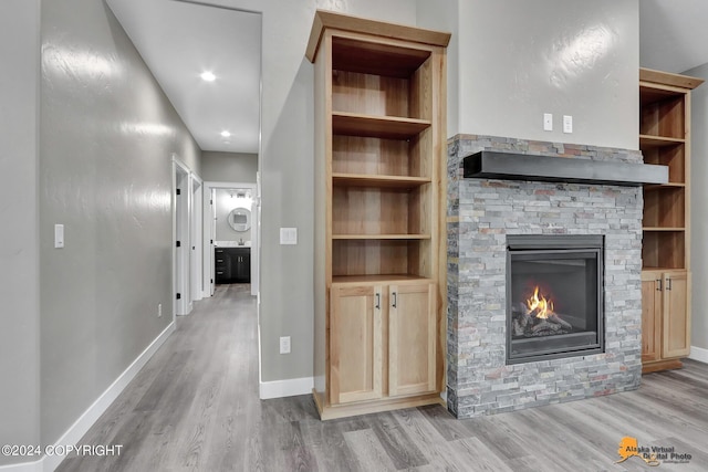 unfurnished living room featuring built in shelves, a stone fireplace, and light hardwood / wood-style floors