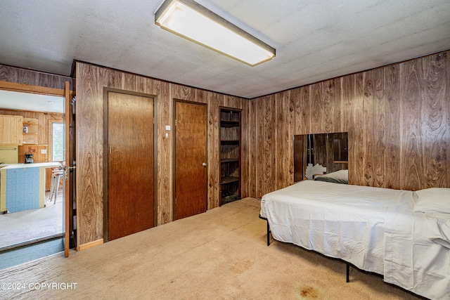 bedroom featuring two closets, carpet flooring, a textured ceiling, and wood walls