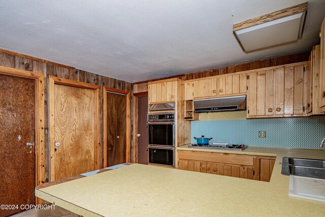 kitchen with gas stovetop, wood walls, a textured ceiling, kitchen peninsula, and double oven