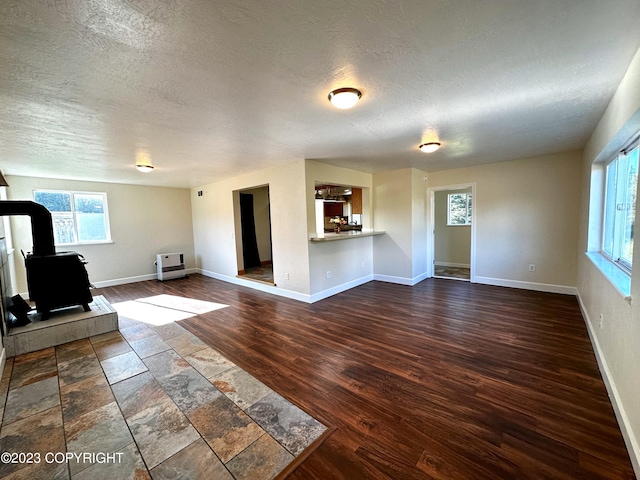 unfurnished living room featuring a textured ceiling, wood-type flooring, and a wood stove