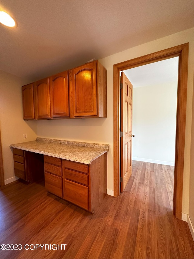 kitchen featuring wood-type flooring, light stone counters, and built in desk