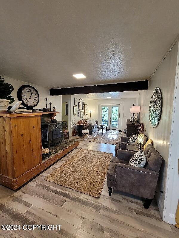 living room with wood-type flooring, a textured ceiling, french doors, and a wood stove