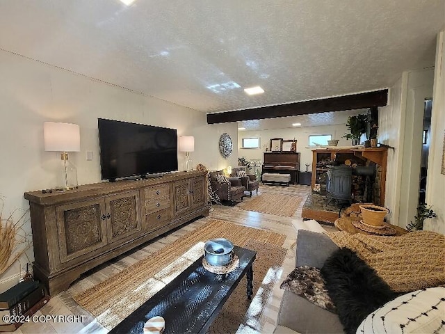 living room with a textured ceiling, light hardwood / wood-style floors, beam ceiling, and a wood stove