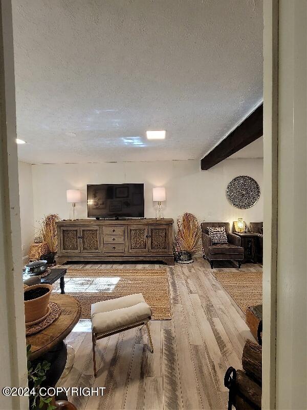 living room with beamed ceiling, a textured ceiling, and light hardwood / wood-style floors