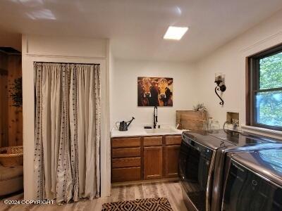 clothes washing area featuring separate washer and dryer, cabinets, light hardwood / wood-style flooring, and sink