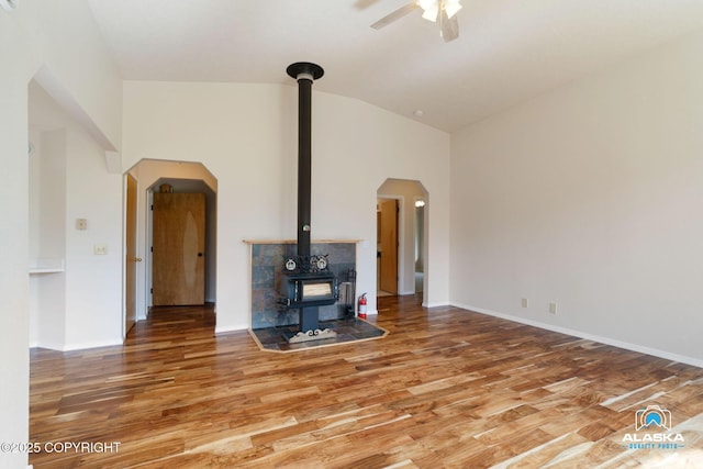 4477 Panther Dr, Eagle River, AK 99577 - unfurnished living room with a wood stove, wood finished floors, a ceiling fan, arched walkways, and high vaulted ceiling