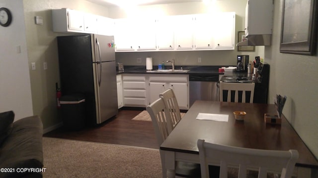 kitchen with a sink, dark countertops, range hood, white cabinetry, and appliances with stainless steel finishes