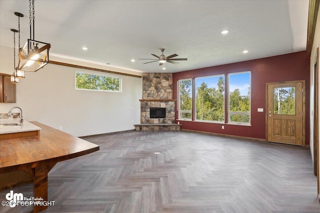 unfurnished living room featuring ceiling fan, sink, a fireplace, and dark parquet floors