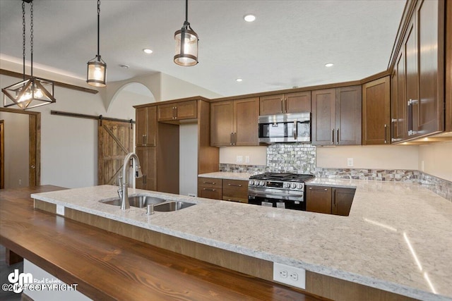 kitchen with a barn door, decorative backsplash, appliances with stainless steel finishes, light stone countertops, and sink