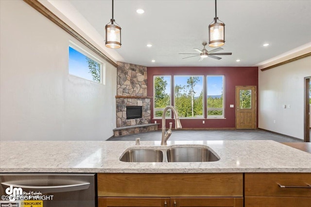 kitchen featuring a stone fireplace, hanging light fixtures, light stone counters, ceiling fan, and sink