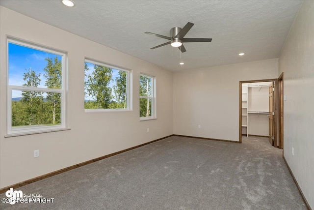 unfurnished bedroom featuring a textured ceiling, carpet, ceiling fan, a spacious closet, and a closet