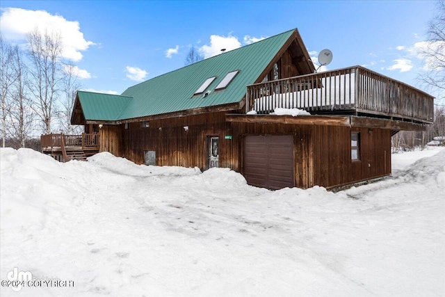 snow covered rear of property featuring a garage, metal roof, and a deck