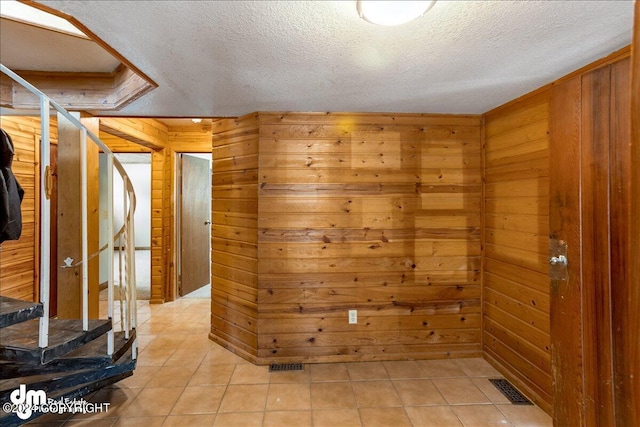 interior space with wooden walls, visible vents, a textured ceiling, and light tile patterned floors