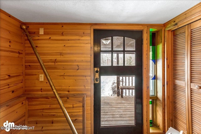 doorway to outside featuring a textured ceiling and wood walls