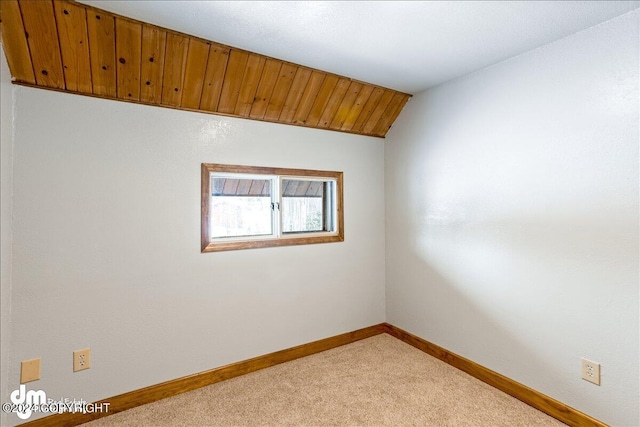 spare room with light carpet, vaulted ceiling, and baseboards