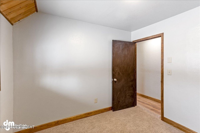 spare room with light carpet, baseboards, and lofted ceiling