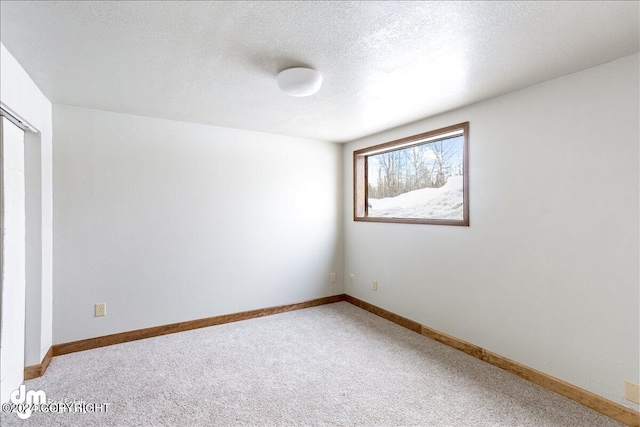 empty room with a textured ceiling, carpet floors, and baseboards