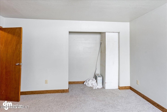 unfurnished bedroom with light carpet, a closet, baseboards, and a textured ceiling