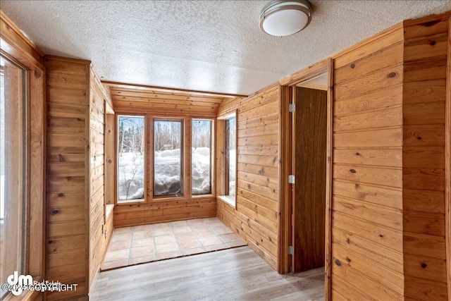 interior space featuring light wood-type flooring, a textured ceiling, and wooden walls