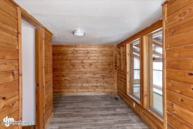 empty room with wooden walls, a textured ceiling, a sauna, and wood finished floors