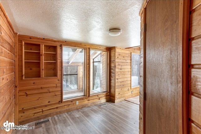 spare room featuring a textured ceiling, wood walls, wood finished floors, and visible vents