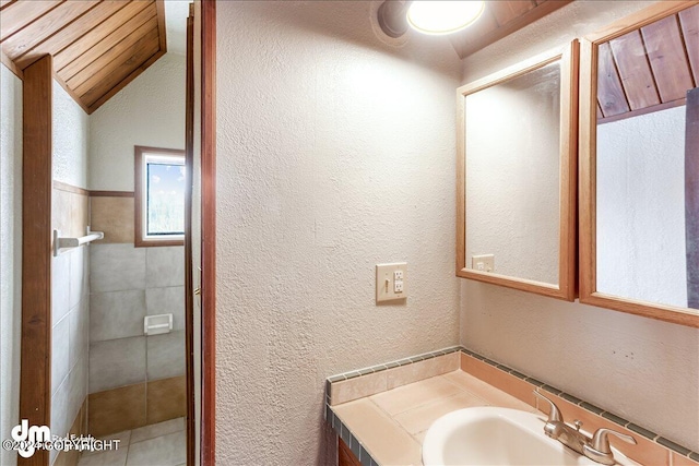 bathroom with lofted ceiling, a sink, and a textured wall