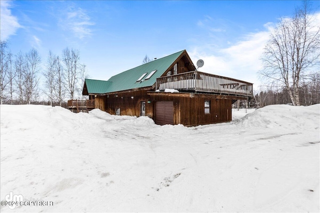 snow covered back of property featuring a garage, metal roof, and a wooden deck