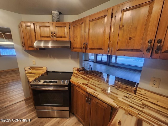 kitchen with brown cabinetry, electric stove, light wood-type flooring, under cabinet range hood, and wooden counters