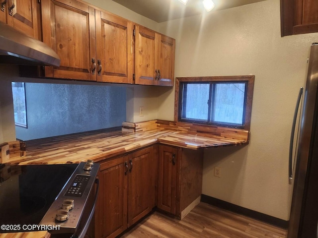 kitchen featuring stainless steel appliances, butcher block counters, brown cabinetry, light wood-type flooring, and extractor fan