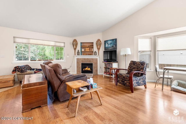 living room featuring a tile fireplace, vaulted ceiling, and light hardwood / wood-style floors