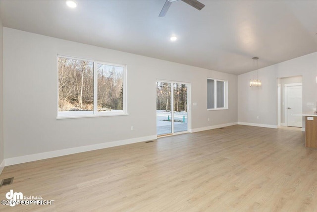 unfurnished living room featuring ceiling fan with notable chandelier, light hardwood / wood-style flooring, and a healthy amount of sunlight