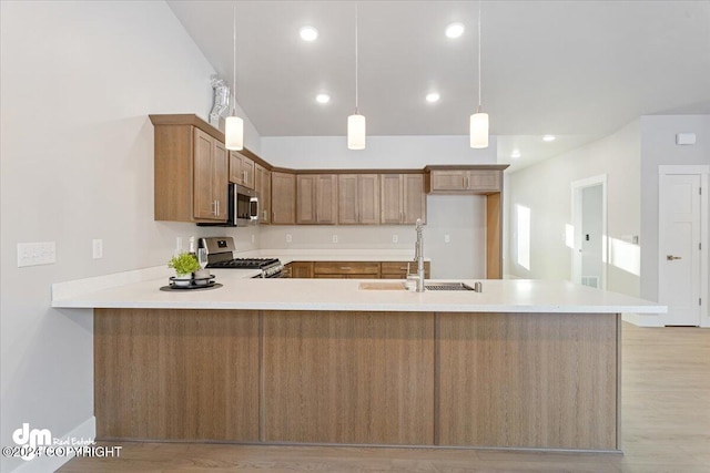 kitchen featuring stainless steel appliances, sink, kitchen peninsula, hanging light fixtures, and light hardwood / wood-style flooring