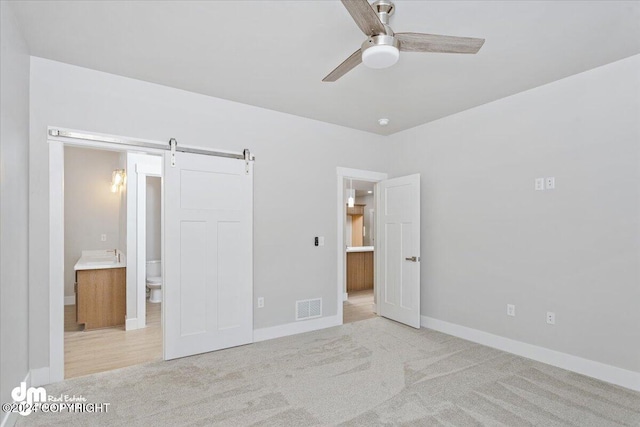 unfurnished bedroom with a barn door, ensuite bathroom, light colored carpet, and ceiling fan