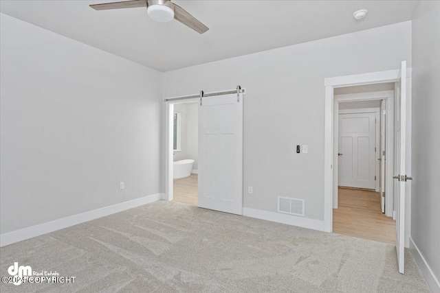 unfurnished bedroom with a barn door, ceiling fan, ensuite bath, and light carpet