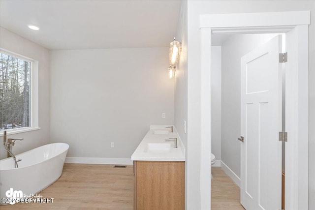 bathroom featuring vanity, wood-type flooring, a tub to relax in, and toilet