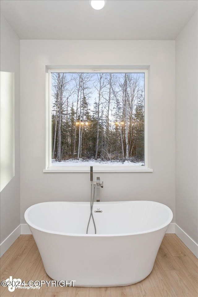 bathroom featuring wood-type flooring, a healthy amount of sunlight, and a bath