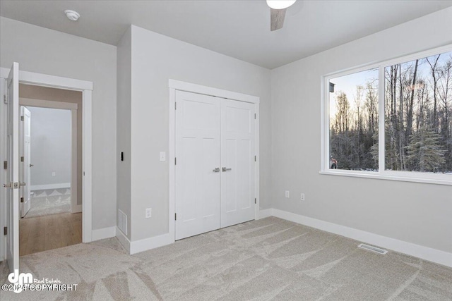 unfurnished bedroom with light colored carpet, multiple windows, ceiling fan, and a closet