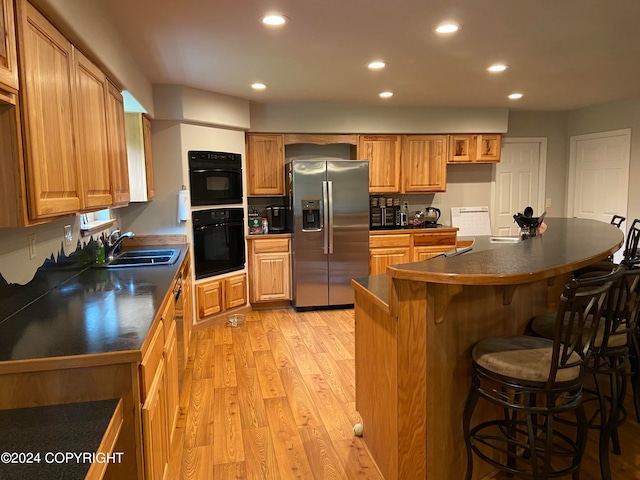 kitchen with sink, light wood-type flooring, stainless steel fridge with ice dispenser, and a kitchen breakfast bar