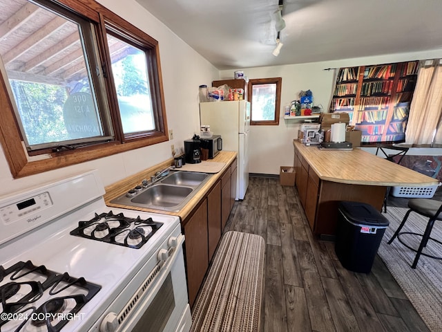 kitchen featuring sink, white appliances, a breakfast bar area, rail lighting, and dark hardwood / wood-style floors