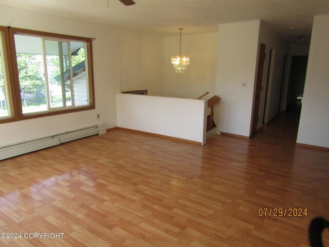 spare room featuring hardwood / wood-style floors, ceiling fan with notable chandelier, and a baseboard heating unit