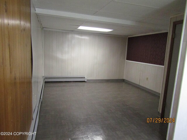 spare room featuring a paneled ceiling, wood walls, and baseboard heating