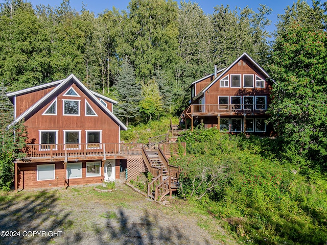 rear view of property with a forest view, stairs, and a deck