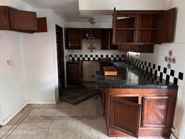 kitchen with dark brown cabinets, backsplash, baseboards, and a sink