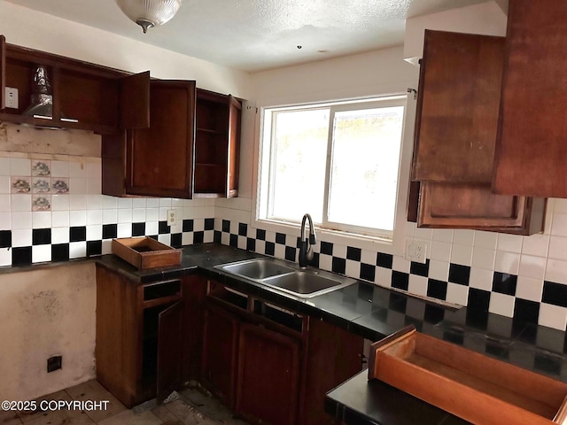 kitchen featuring tasteful backsplash, a textured ceiling, dark countertops, and a sink