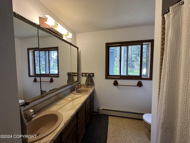 bathroom with a baseboard radiator, toilet, plenty of natural light, and double vanity